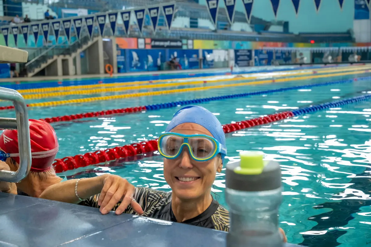 An adult swimmer resting at the wall of an indoor pool after a length